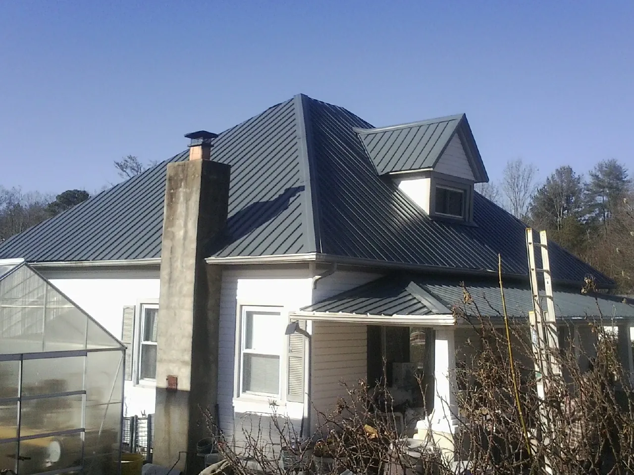 Dark blue standing seam metal roof on a white farmhouse with dormer — Slate & Tile Roof Repair by Roofing Brothers in Hinckley