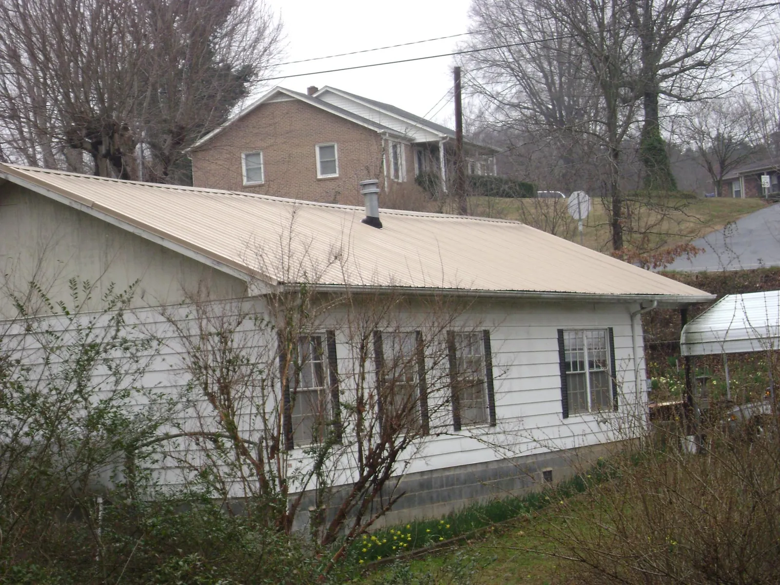 Tan metal roof on a white sided house set into a hillside — Commercial Roofing by Roofing Brothers in Hinckley